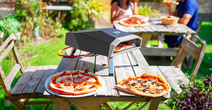 Large image of Luna 12 pizza oven on a table in sunlight with two pizzas, and a couple enjoying pizza in the background